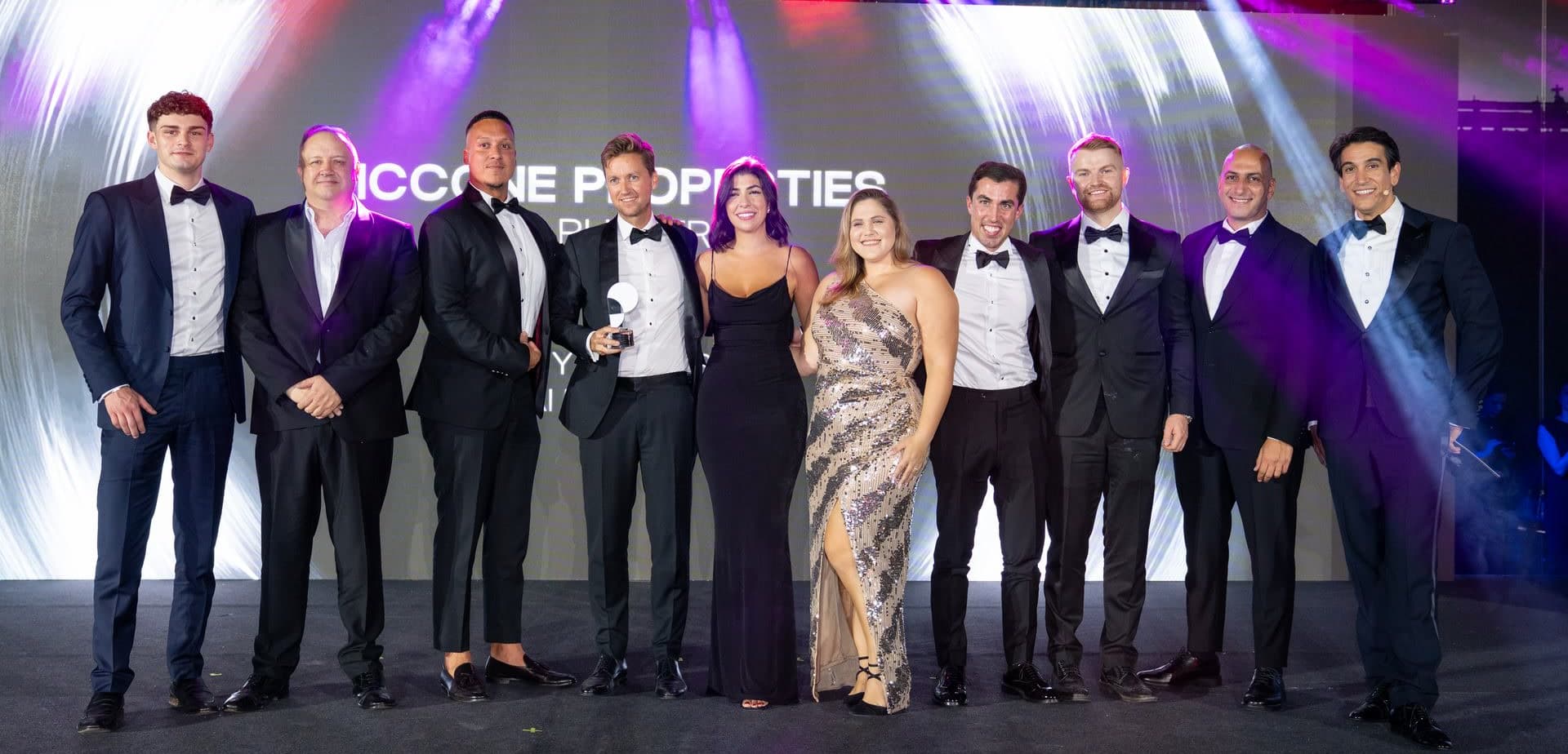 Eleven of the McCone Properties team in black tie on stage at the Property Finder Awards, one of them holding the award