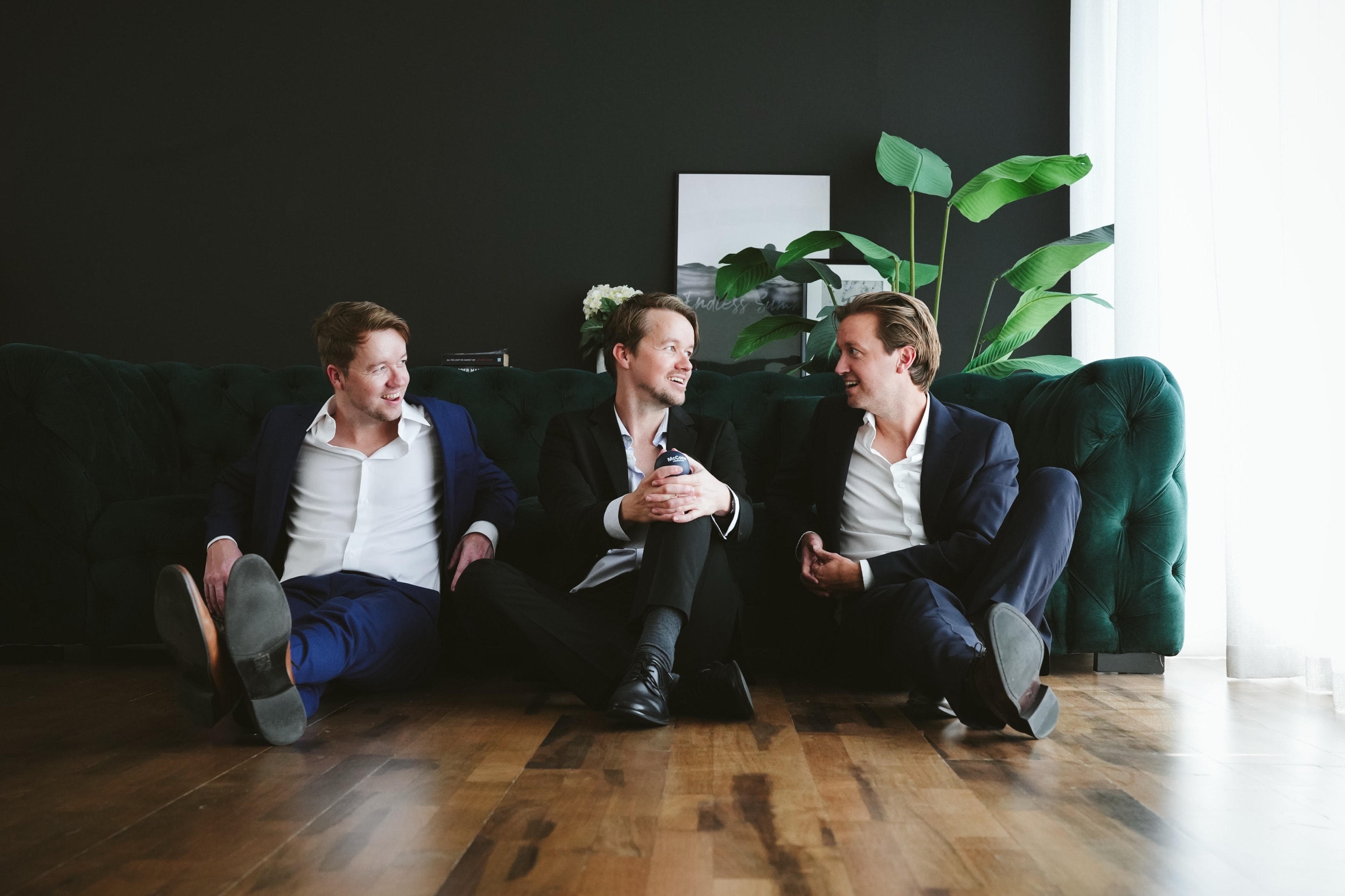 The three McCone Properties partners sitting together on the office floor in front of a green velvet sofa